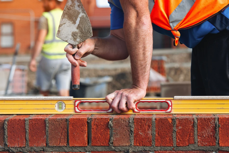 Un ma&ccedil;on qualifi&eacute; v&eacute;rifie le niveau de briques fra&icirc;chement pos&eacute;es sur un chantier de construction &agrave; la lumi&egrave;re du soleil de l'apr&egrave;s-midi