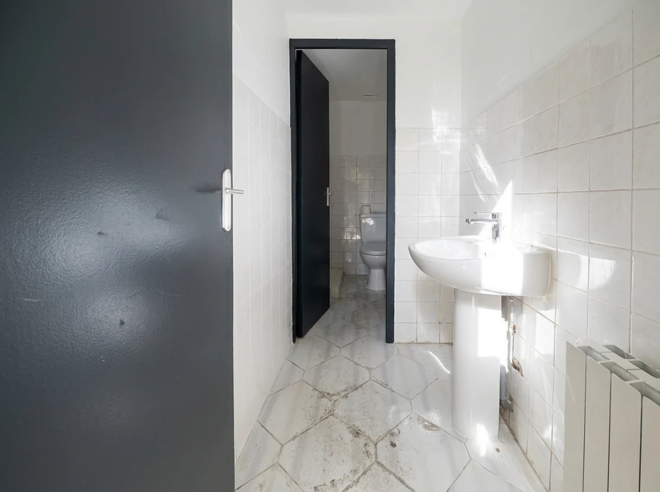 Salle de bain étroite non meublée, carrelage mural blanc brillant, sol en carreaux hexagonaux marbre clair encrassés