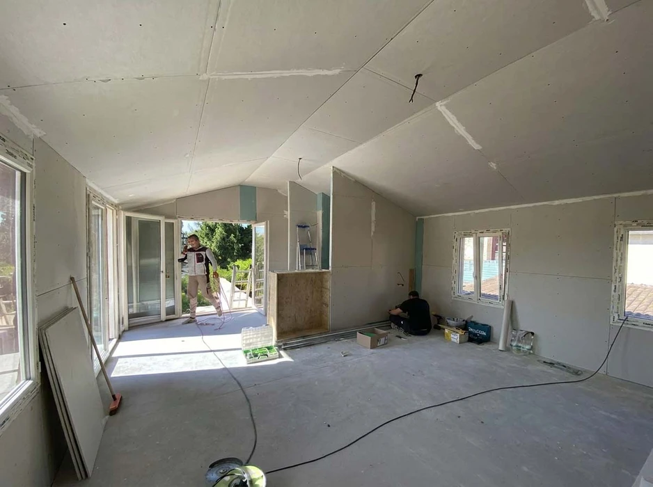 Chantier intérieur en cours, deux ouvriers travaillent dans une pièce principale