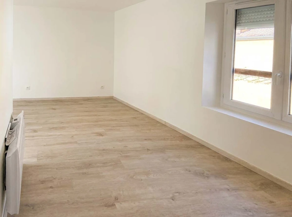 Ouvrier en tenue professionnelle appliquant un crépi ou un enduit de façade sur un mur extérieur d'une maison, utilisant une taloche ou une truelle, avec traces de finition visible sur la surface du mur. La scène se déroule à l'extérieur en plein jour, montrant les différentes étapes de la technique de crépissage, activité de spécialisation notée de AEB Bâtiment.