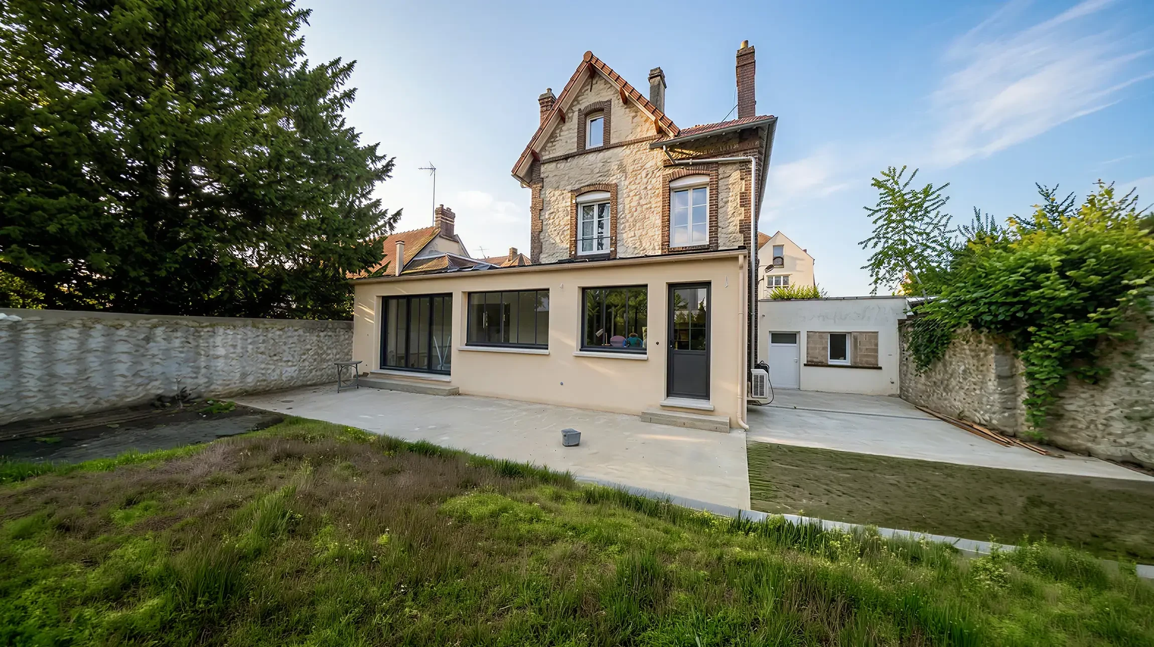 Un ouvrier du bâtiment, portant des gants et une ceinture d'outils, soulève des poutres en bois tout en naviguant à travers un espace intérieur partiellement construit