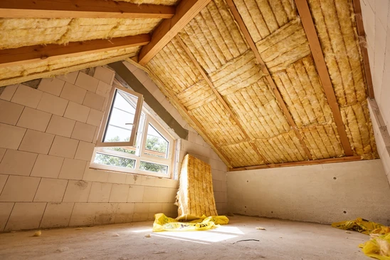 Ouvrier en combinaison de protection int&eacute;grale et masque respiratoire installant de l'isolant thermique jaune dans les combles d'une habitation