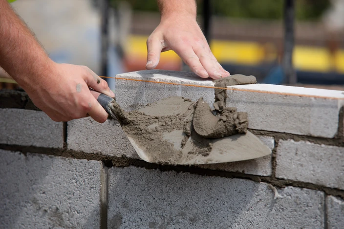 Ouvrier en bâtiment construisant un mur en parpaings à l'extérieur, utilisant un niveau à bulle pour vérifier l'alignement